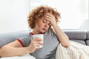 wegovy side effects | woman on sofa with tea with her hand to her forehead
