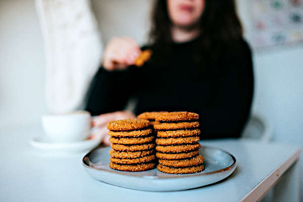 foods to avoid on wegovy | biscuits on table in foreground with woman sitting on chair with coffee